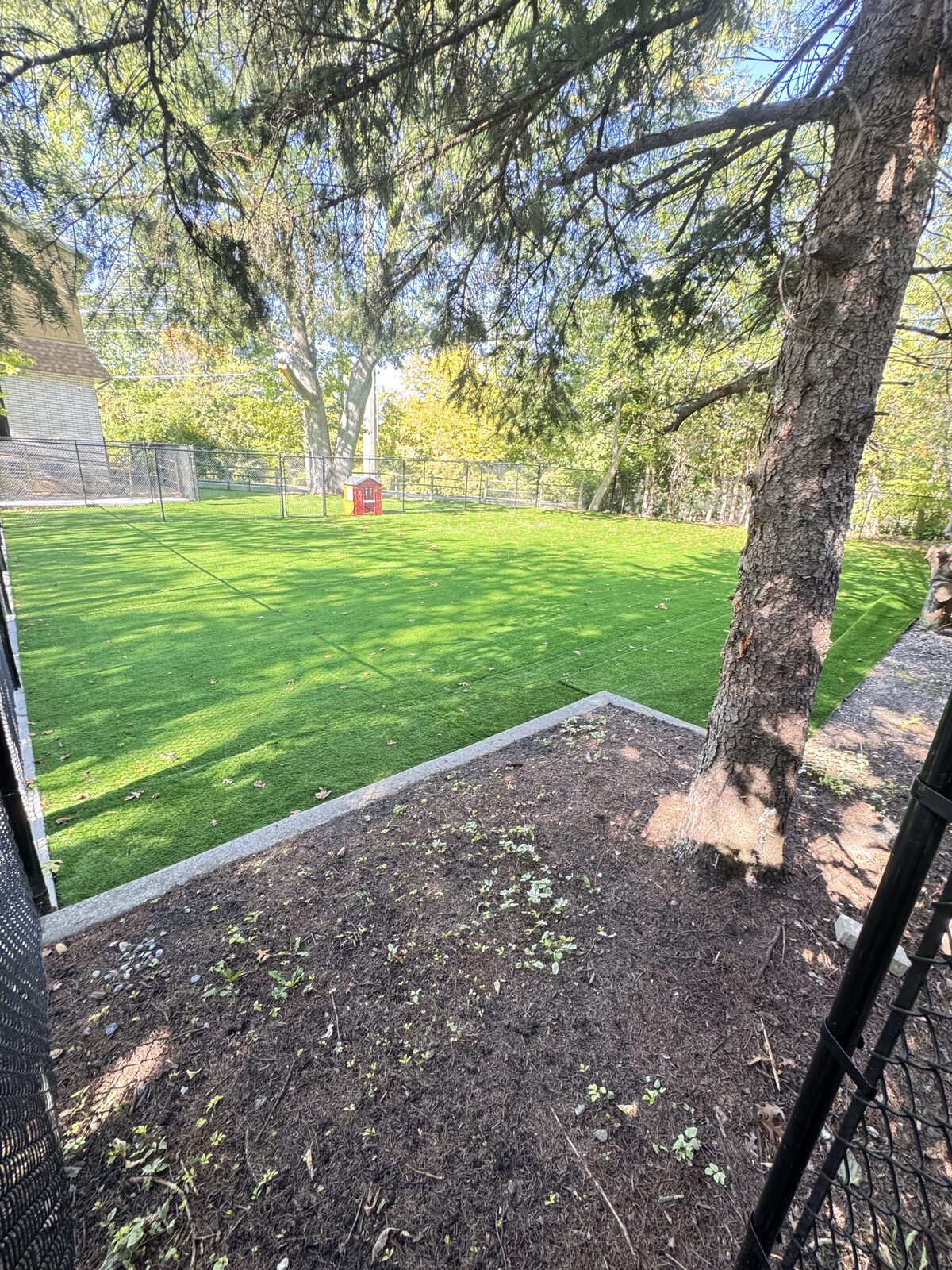 Concrete border around a fenced backyard with new turf and a small red playhouse.