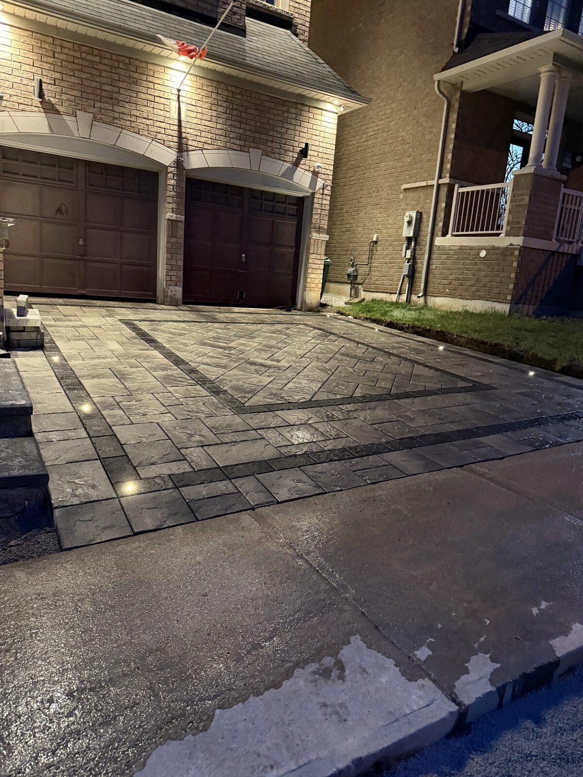 Decorative interlocking stone driveway with lighting beside a garage.