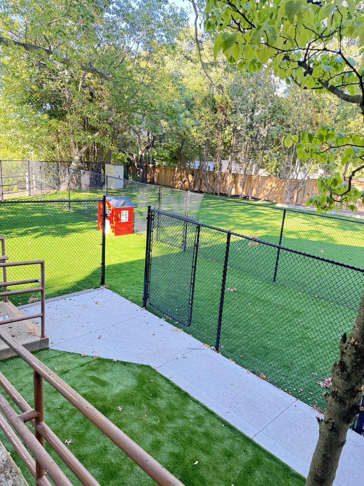 Concrete walkway leads to a fenced artificial grass area with a dog house.
