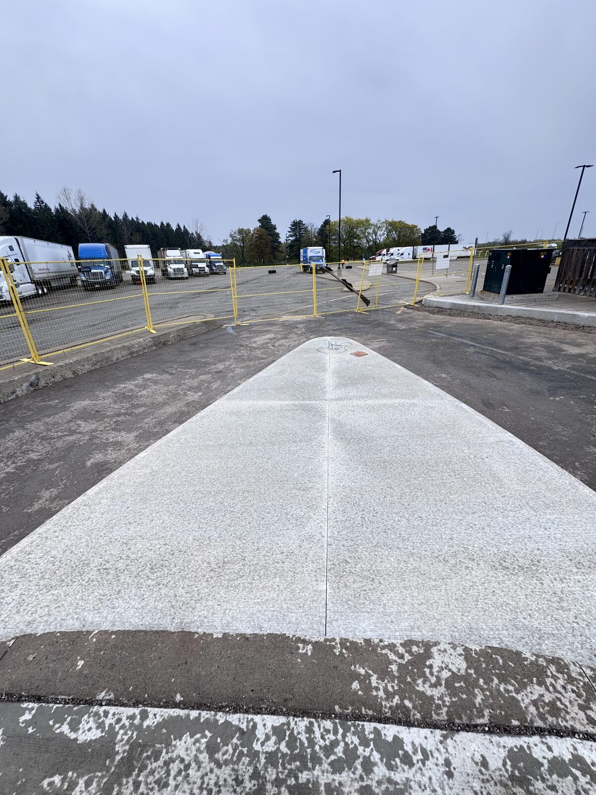 New concrete apron in a truck parking area with yellow safety fencing.
