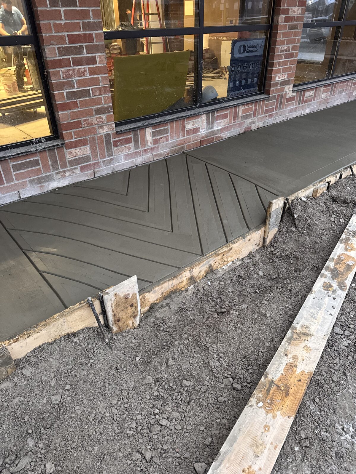 Freshly poured concrete walkway with chevron pattern in front of brick building
