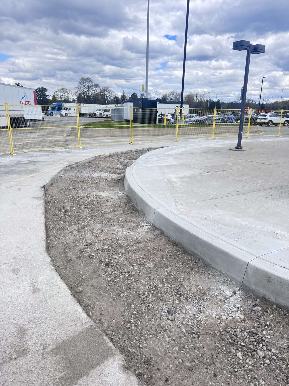 Curved concrete curb and sidewalk under construction with temporary fencing.