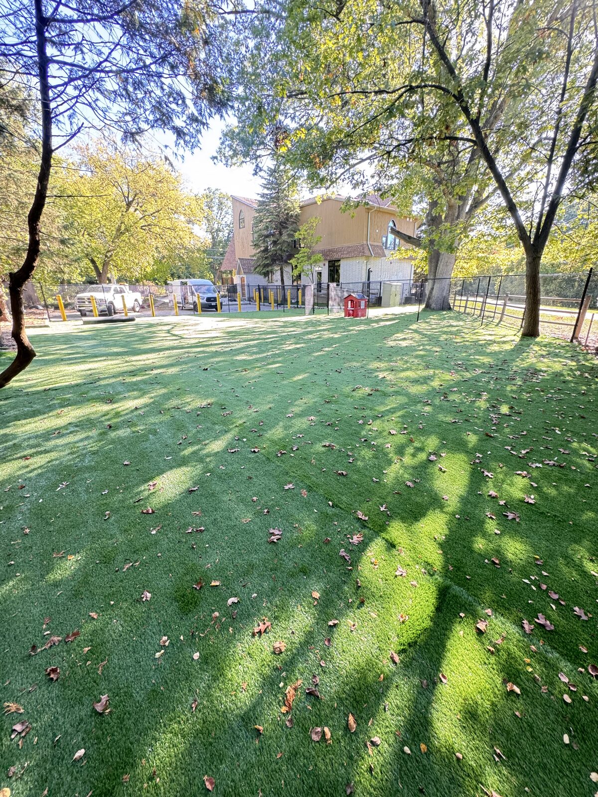 Artificial turf dog park with fencing and a building structure.