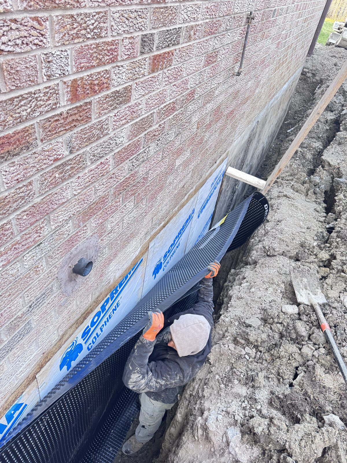 Worker installing waterproofing membrane on a brick foundation wall