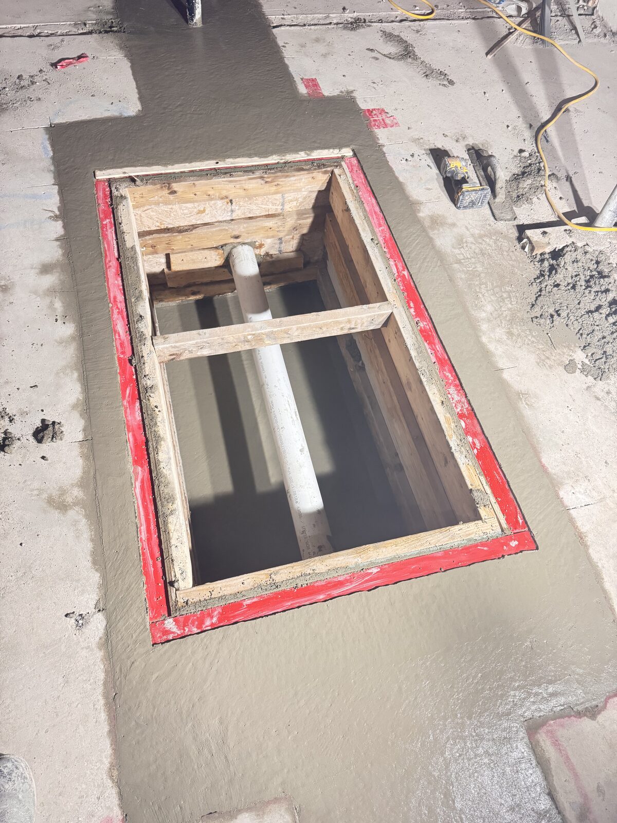 Concrete pour around a newly installed drainage pipe with wooden framing.