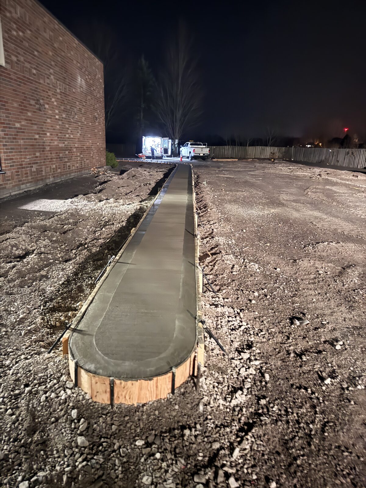 Newly poured concrete walkway with curved wooden forms at night.