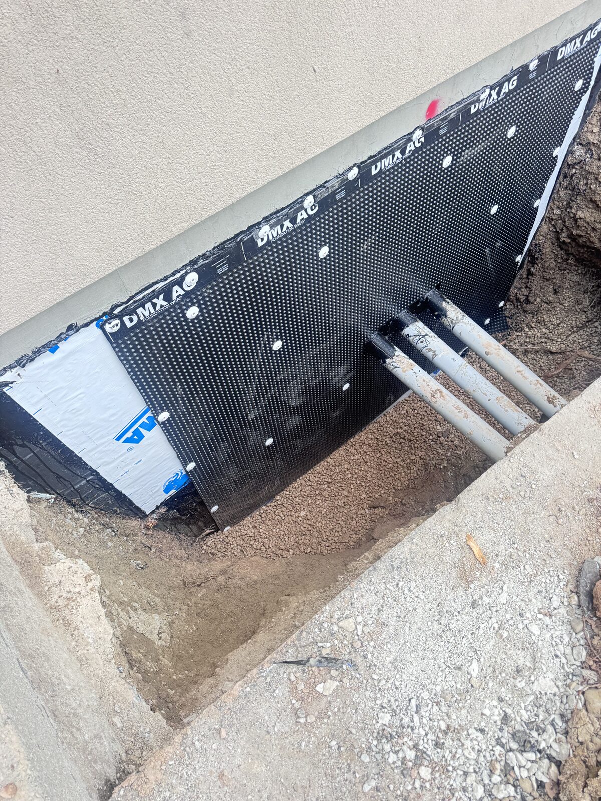 Foundation waterproofing membrane installation with drainage pipes visible