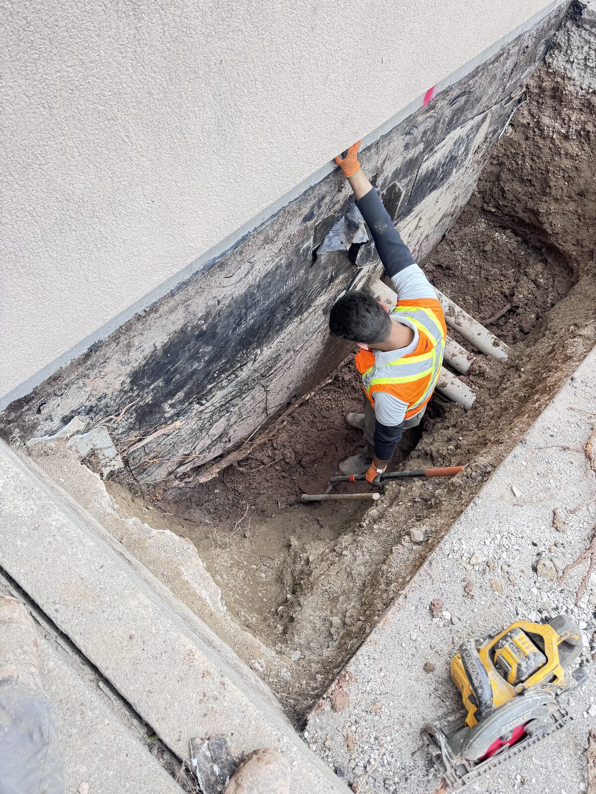 Crew waterproofing foundation walls during excavation and pipe work.