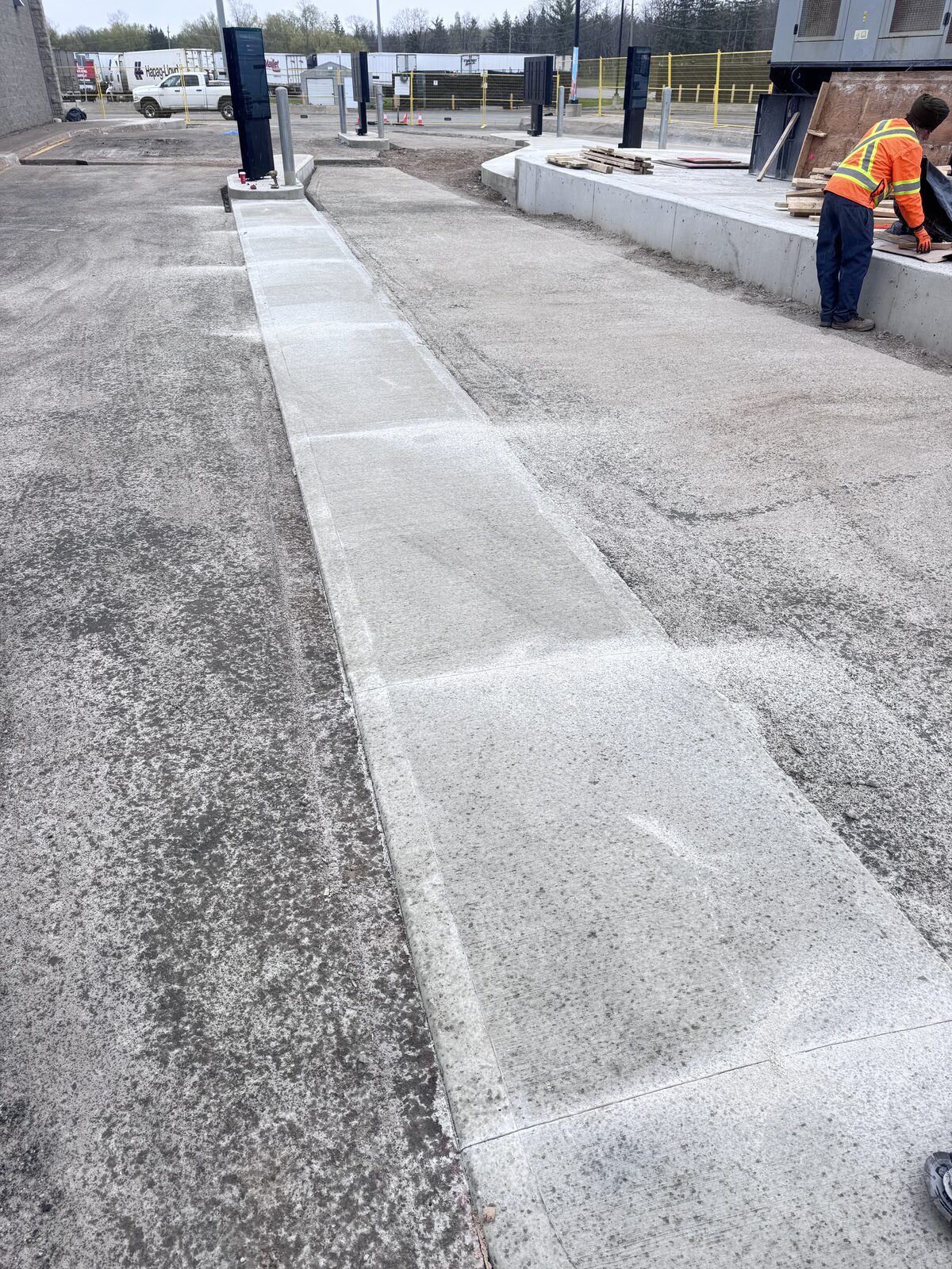 Newly poured concrete walkway next to asphalt area outside a commercial building.