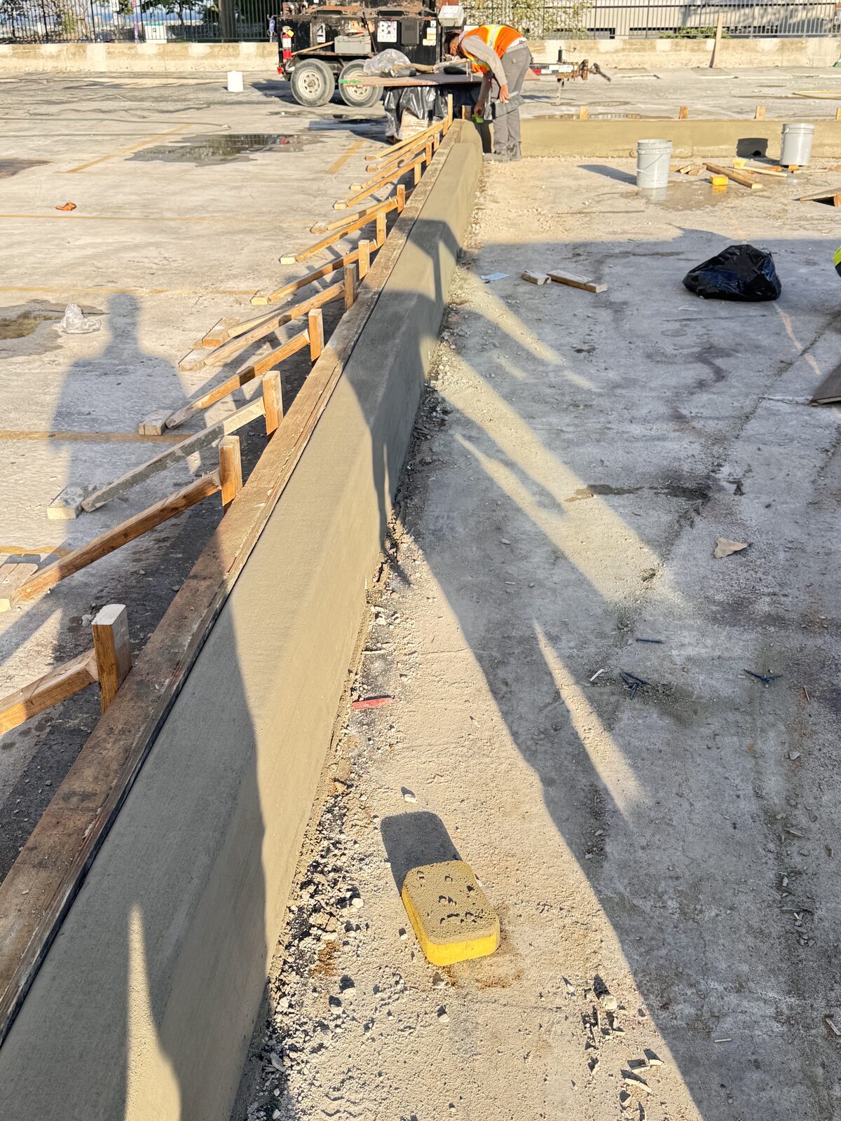 Freshly poured concrete curb construction with wooden forms and workers.